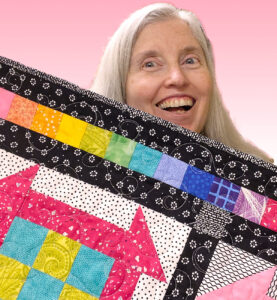 Woman holding a colorful quilt made from the Patching the Hole in the Barn Door block of the week quilt series.