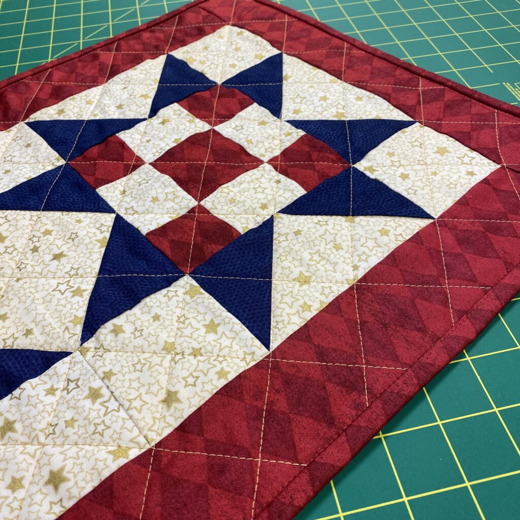 Photo of quilted table runner featuring three blue sawtooth stars with red and white nine-patch centers by Stacy Creates Stuff