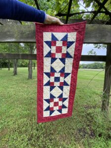 Photo of quilted table runner featuring three blue sawtooth stars with red and white nine-patch centers.