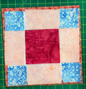 A nine-patch block with a larger dark pink center, light pink rectangles on the sides, and light blue squares in the corner.