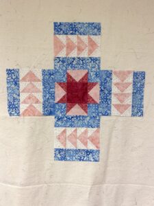 Five quilt blocks on a design wall with one center block (sawtooth star) and four flying geese blocks surrounding it.