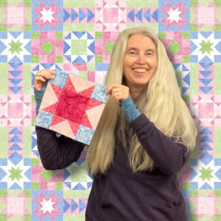 Stacy holding block one of the Stars in My Garden series, a pink sawtooth star block with blue corners.