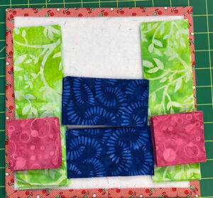 blue, pink, and green pieces of fabric that will become a flying geese block