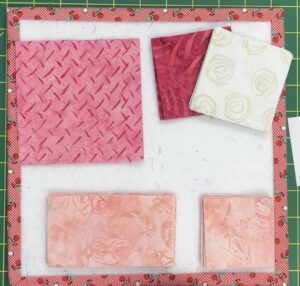 Stacks of pink fabrics cut into squares to make a quilt block