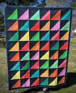Colorful triangle strip quilt with bold navy accents and fan-shaped quilting, displayed outdoors.
